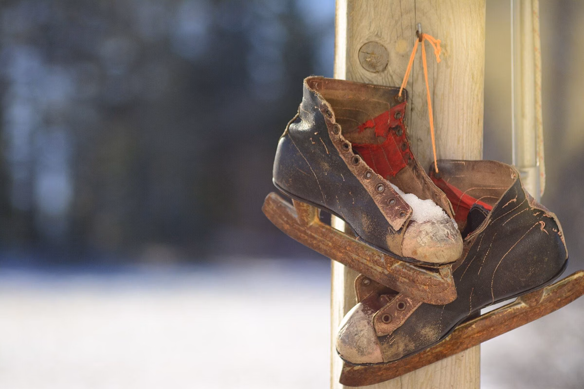 A pair of old leather ice skates hanging by their laces against a snowy background