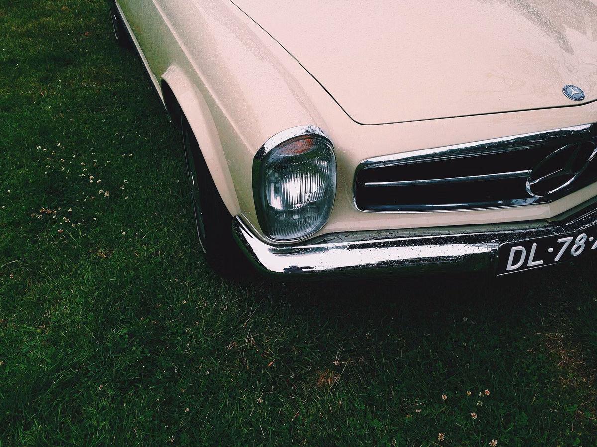The chrome headlight and grille of a pale pink classic convertible parked on grass