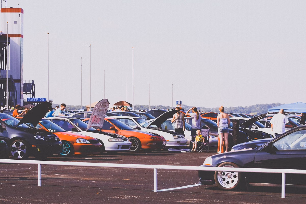 Visitors walking among parked cars at an outdoor car show on a grassy field