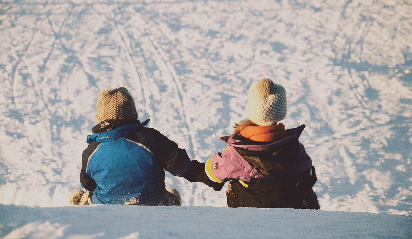 Two children in winter hats and coats sitting together in deep snow