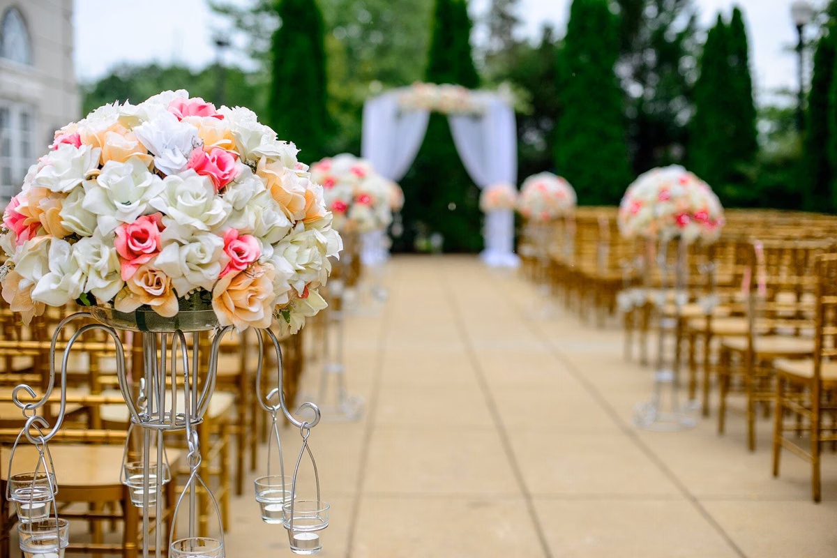 Rows of white chairs and flower arrangements lining the aisle of an outdoor wedding ceremony